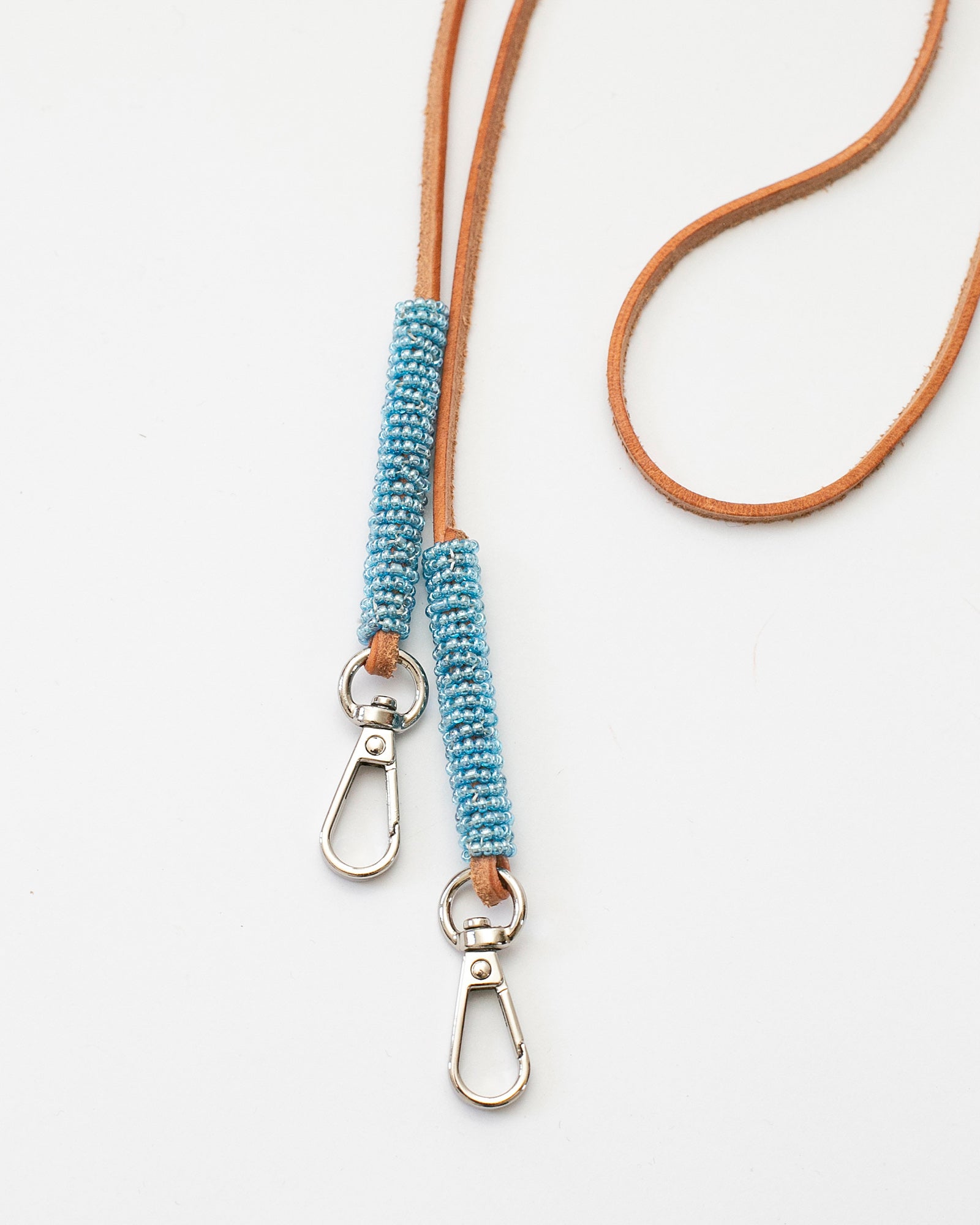 Bandoulière fine en cuir brun ornée de perles bleu clair, modèle "Charo" conçu pour être amovible et adaptable à un sac ou une coque de téléphone. Accessoire élégant, réalisé à la main par un artisan au Kenya, disponible en deux longueurs (90 cm et 110 cm).